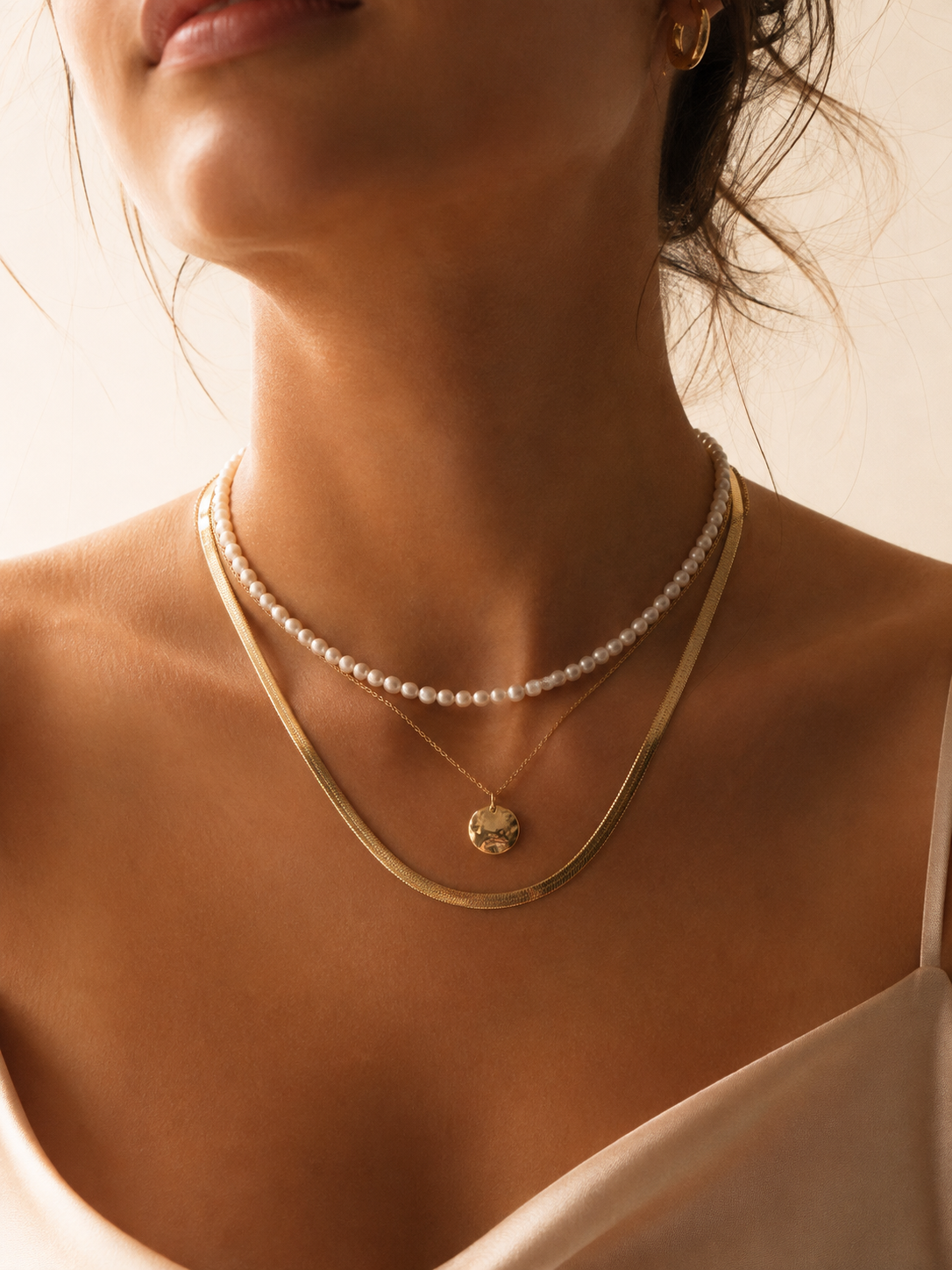 Model wearing layered pearl and gold necklaces